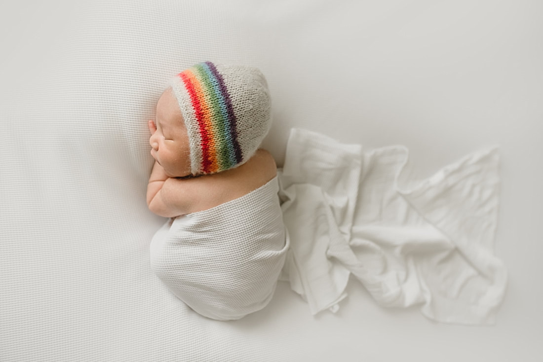 newborn baby boy wearing a rainbow bonnet during newborn photo shoot