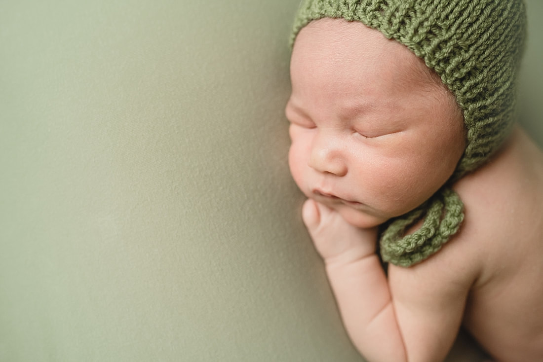 adorable newborn baby boy wearing green bonnet during newborn photo shoot