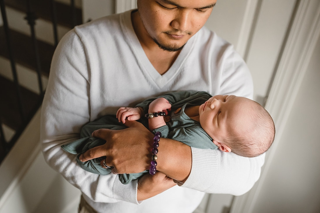dad holding newborn baby boy wearing matching bracelets during newborn photos in memphis tn
