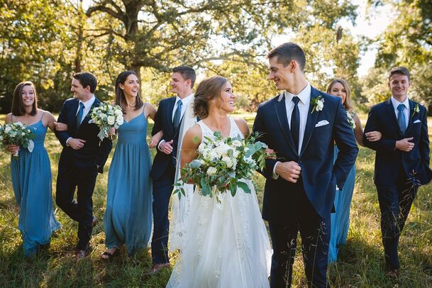 Bride and Groom walking arm in arm with wedding party behind them in an open field during wedding portraits with Sarah Morris Photography in Collierville, TN + Wedding photographers Memphis