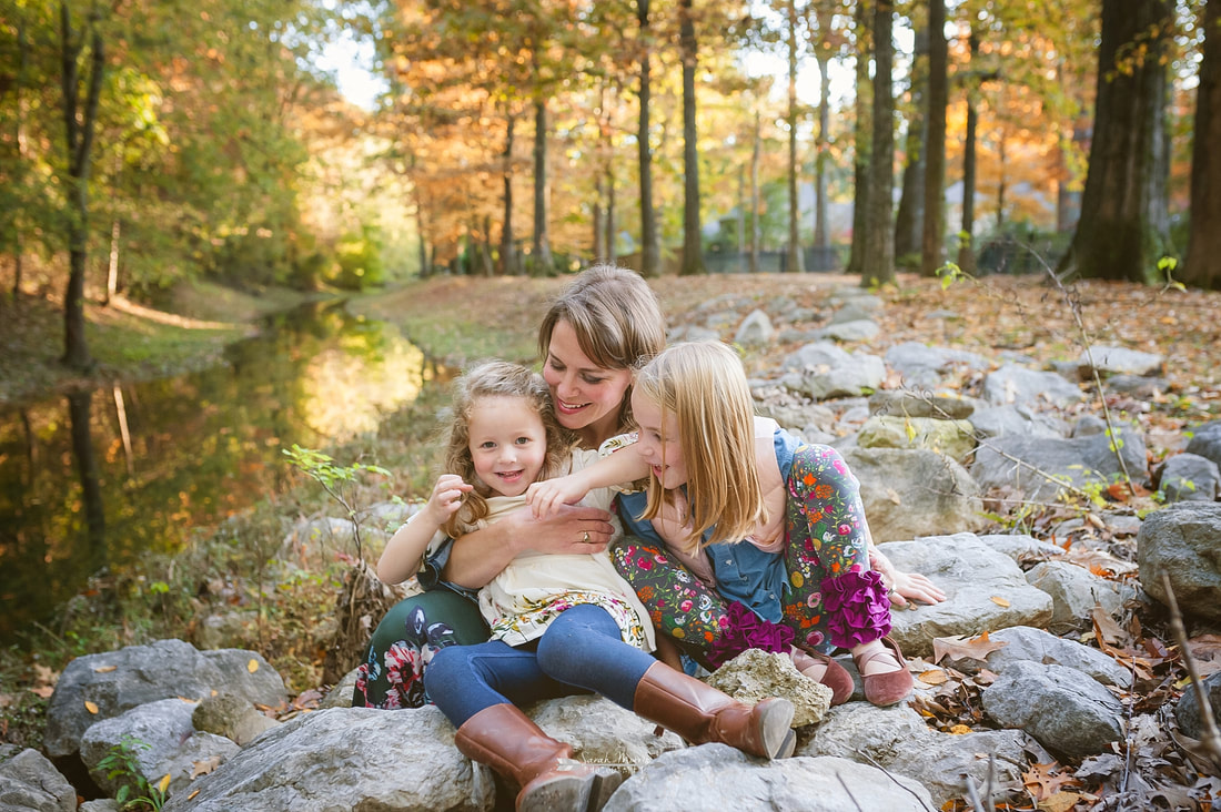 mom snuggling her daughters next to the creek fall family photos
