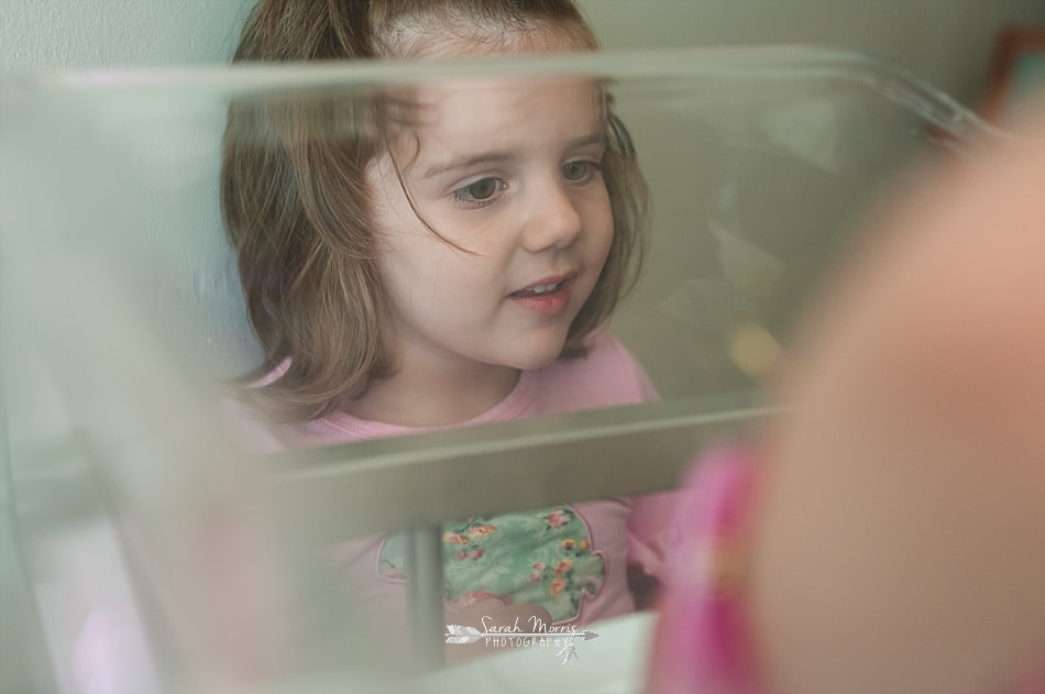 Big sister peeking through the side of her baby sister's bassinet at Methodist Le Bonheur Germantown Hospital