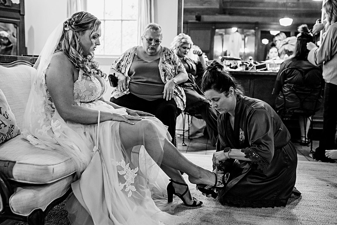 maid of honor helping bride get her wedding shoes on in Green Frog Farm