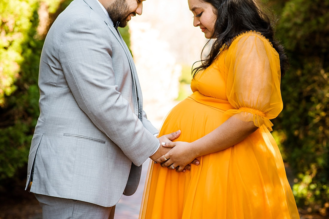 expectant mother and father looking down at pregnant belly during maternity photos at memphis botanic garden