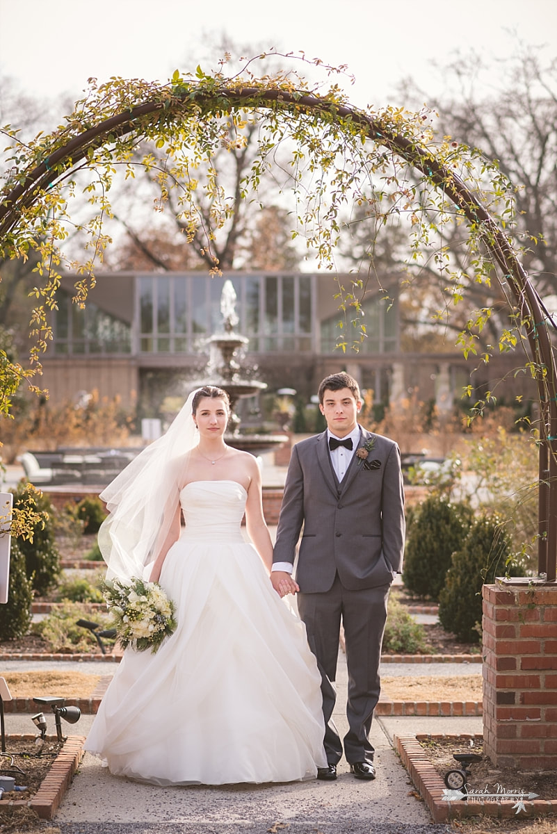 bride and groom holding hands under trellis in the rose garden at memphis botanic garden