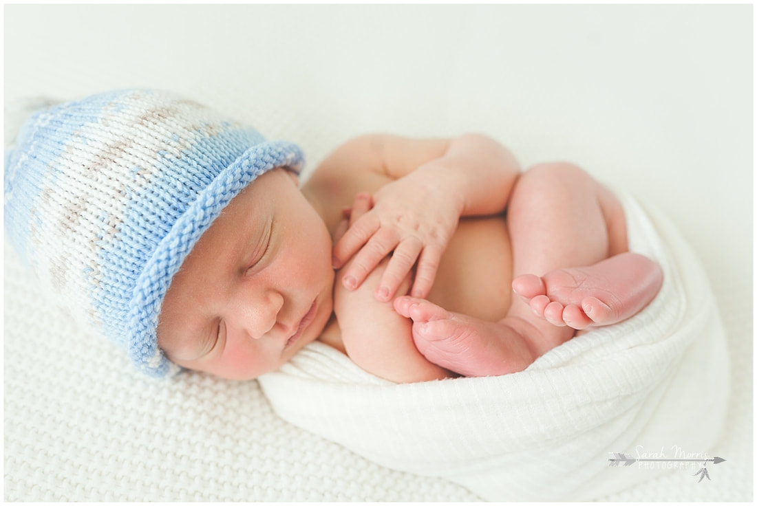 Newborn photo of baby boy sleeping on white blanket wearing blue hat