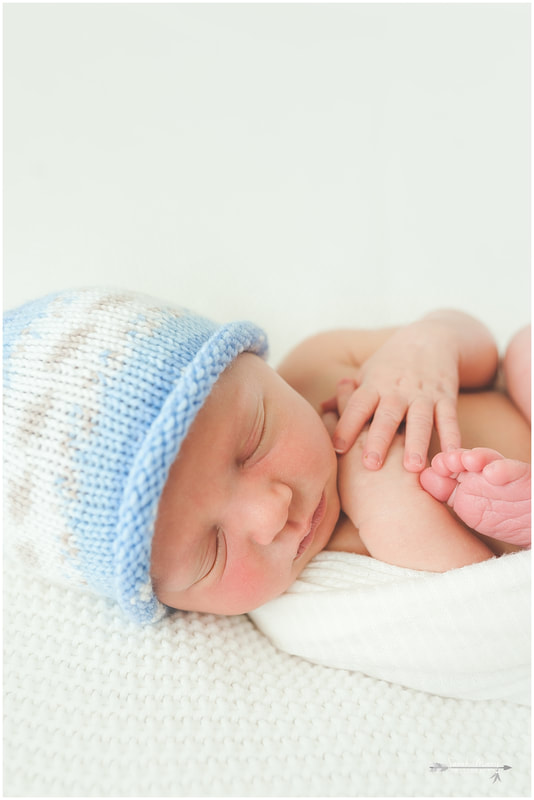 Newborn photo of baby boy sleeping on white blanket wearing blue hat