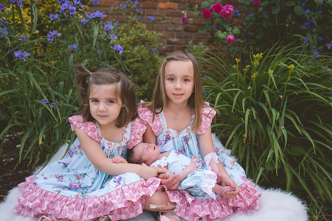 Big sisters holding their newborn baby sister in the flowers