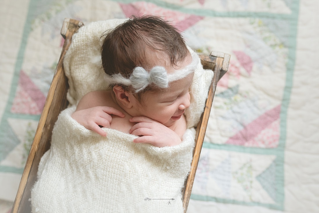 newborn baby girl wearing a bow, wrapped in a cream blanket, sleeping in a rustic wooden box on top of a vintage quilt