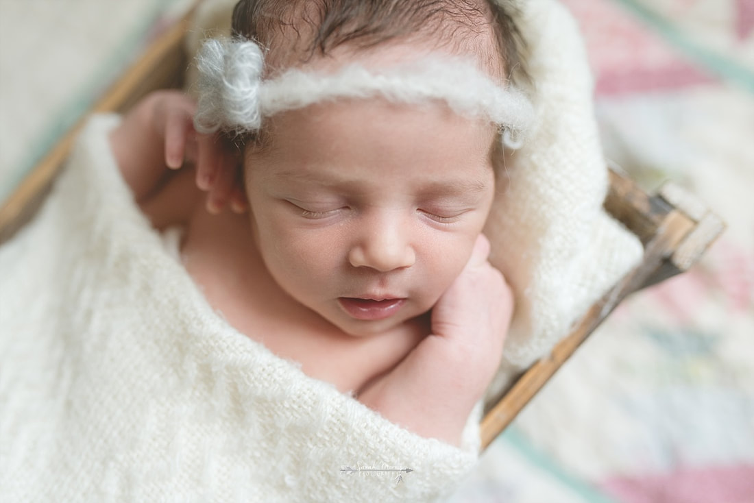 newborn baby girl wearing a bow, wrapped in a cream blanket, sleeping in a rustic wooden box on top of a vintage quilt