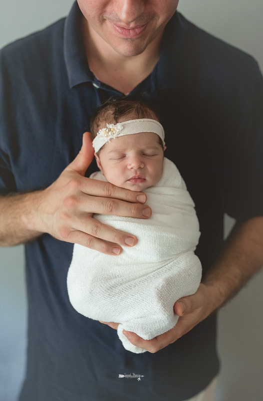 Newborn baby girl in her daddy's hands and swaddled in a cream blanket