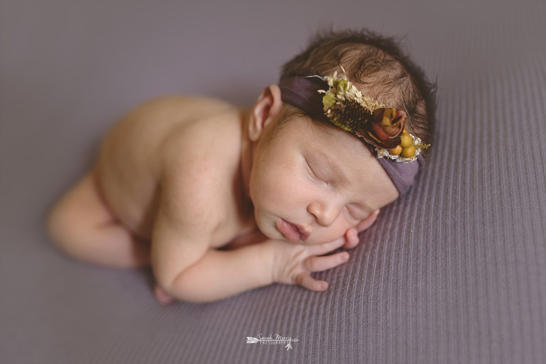 newborn baby girl sleeping on a purple blanket, wearing a purple flower crown