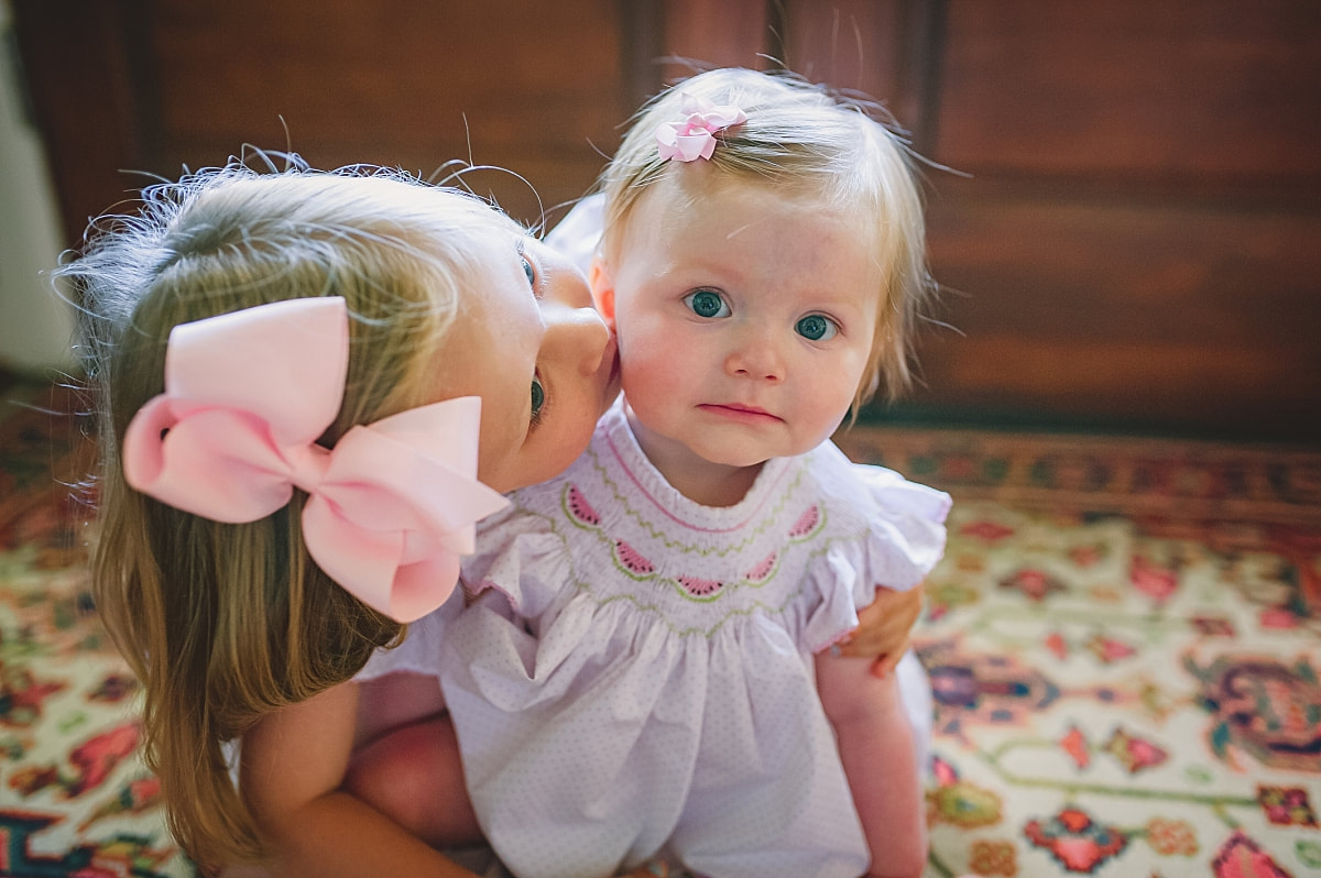 big sister kissing baby sister on the cheek during in home lifestyle family session in collierville, tn