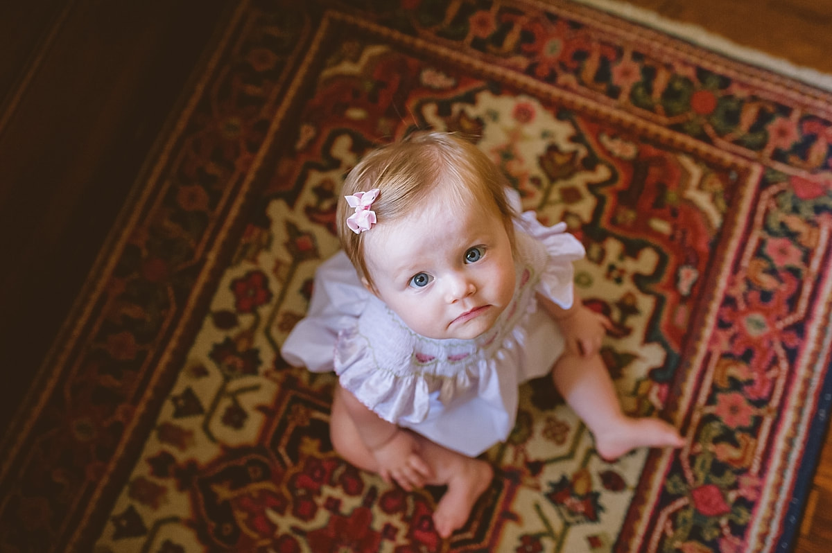 baby girl with blue eyes, sitting on a beautiful oriental rug during in home lifestyle family session in collierville, tn