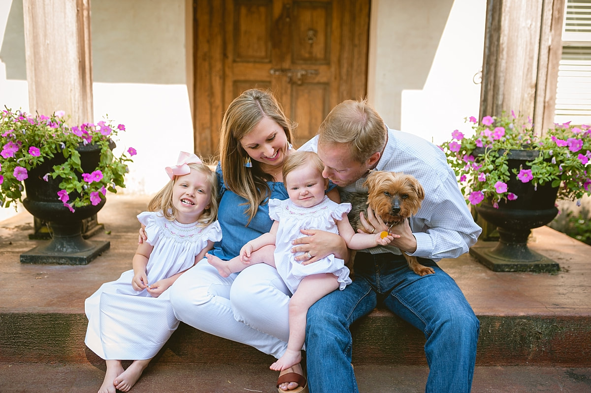 mom and dad snuggling baby girls on their front porch during in home lifestyle family session in collierville, tn