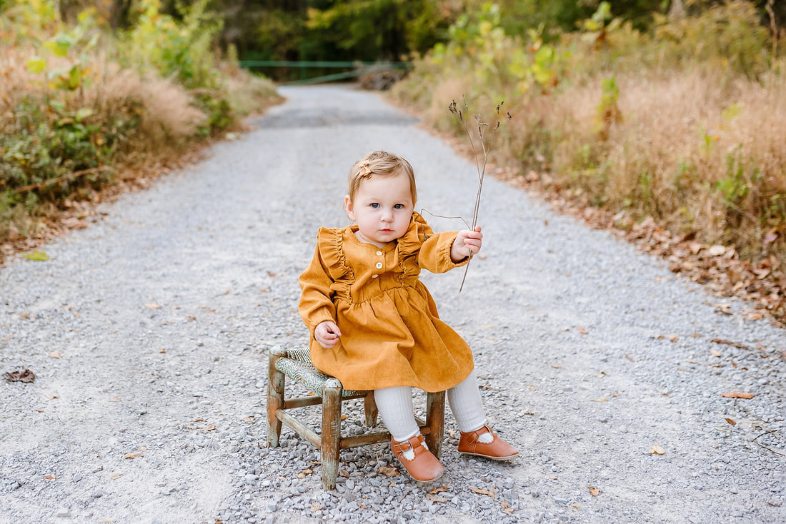 child holding a bright yellow leaf over one eye during fall mini session in collierville, tn