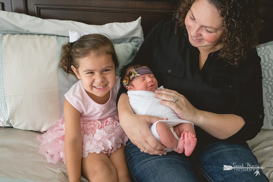 Mom cuddled up on bed with newborn baby sister for the lifestyle portion of her newborn photo session