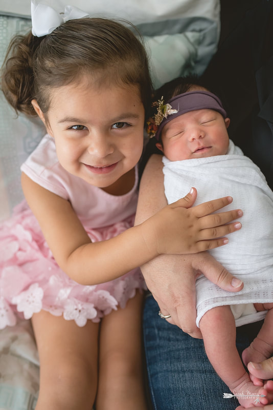 Close up of sisters while the family is cuddled up on bed with newborn baby sister for the lifestyle portion of her newborn photo session