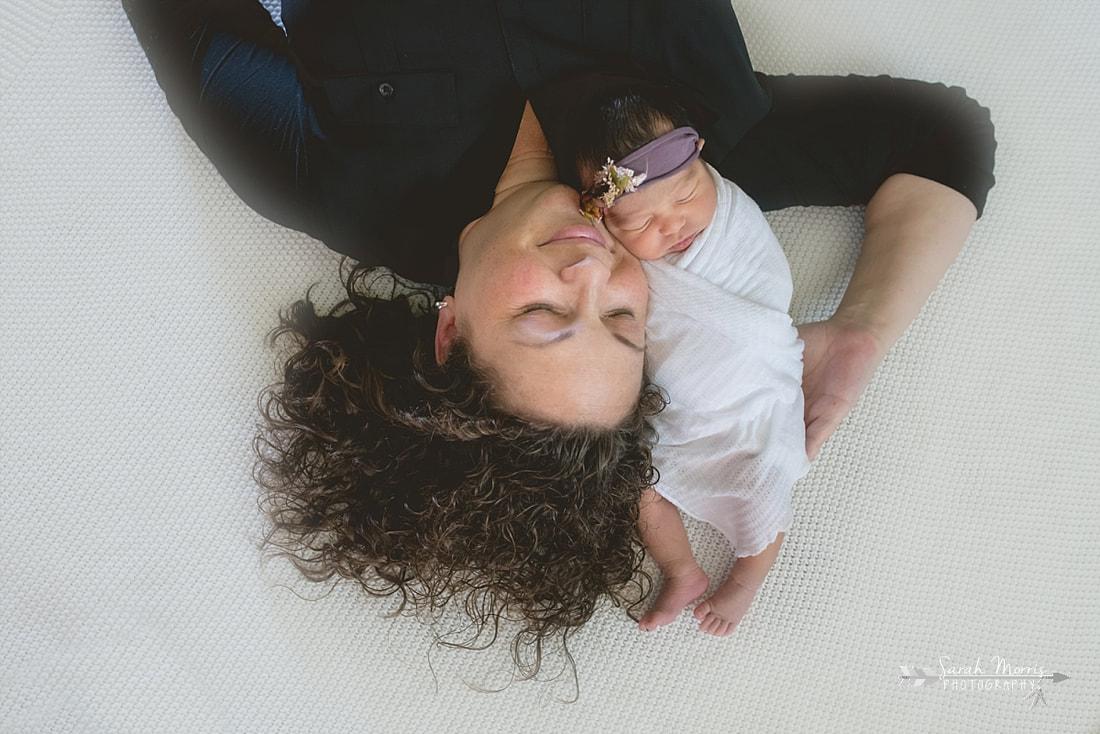 Mother holding baby girl on white blanket during the lifestyle portion of her newborn photo sessionPicture