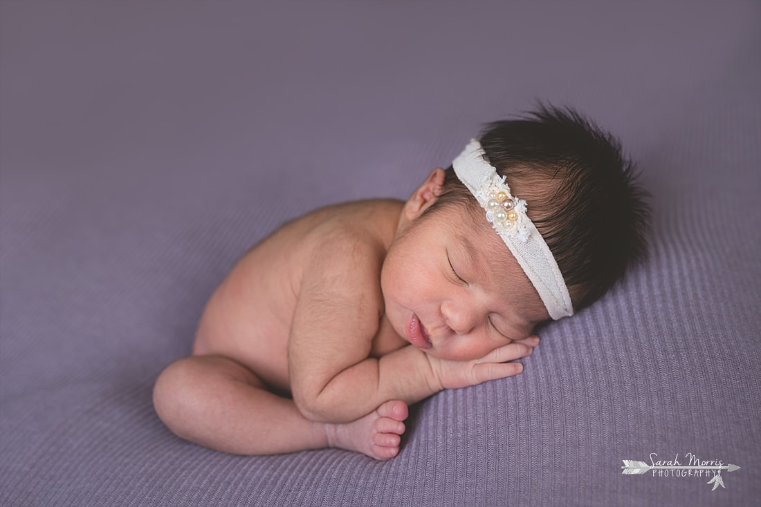 Newborn baby girl wearing a cream headband with pearls sleeping on purple blanket during the posed portion of her newborn session