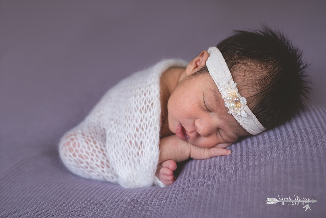 Newborn baby girl wearing a cream headband with pearls and wrapped in a beautiful soft cream knit blanket sleeping on purple blanket during the posed portion of her newborn session