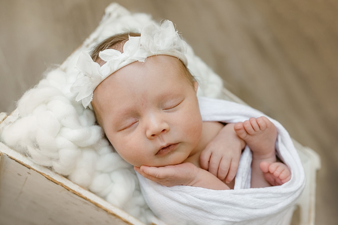 baby girl wrapped in white blanket, sleeping in basket for newborn photos in Memphis, TN