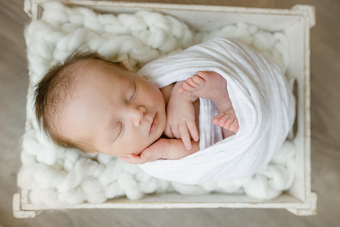 baby girl swaddled in white blanket, sleeping in basket for newborn photos in Memphis, TN