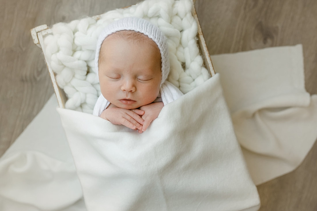 baby girl swaddled in white blanket, sleeping in basket for newborn photos in Memphis, TN
