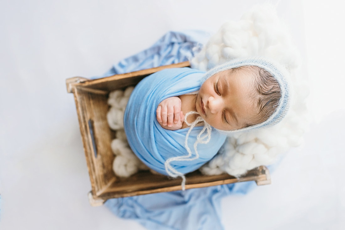 newborn baby boy wrapped in blue blanket sleeping in wooden prop for newborn photo session in memphis