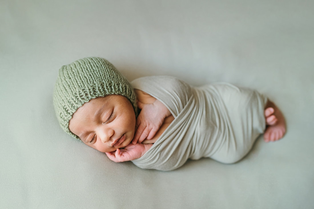 newborn baby boy wearing green knit bonnet wrapped in green blanket for newborn photos in memphis