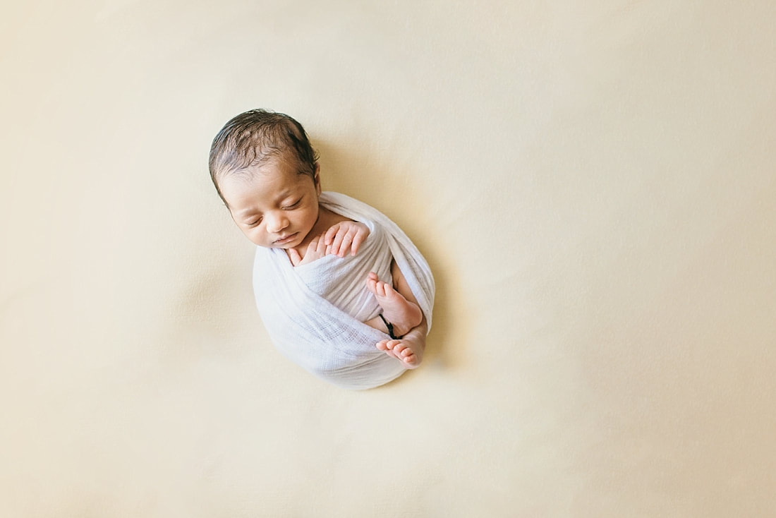 newborn baby wrapped in white on yellow background for newborn photos in memphis