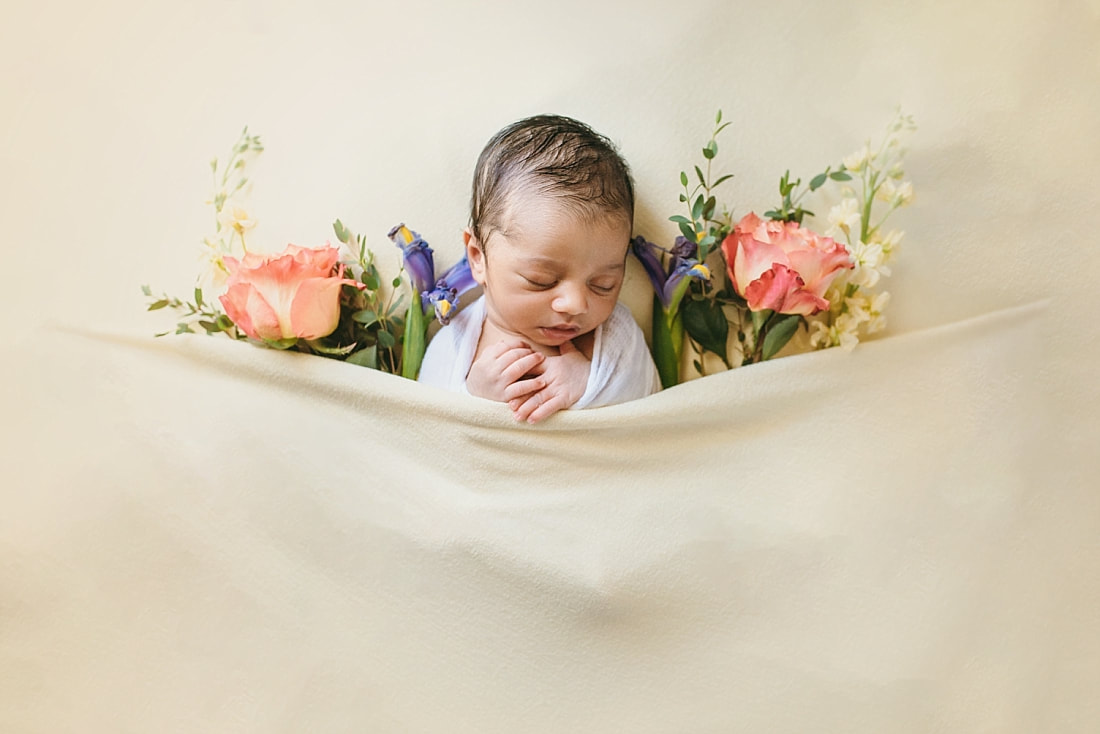 newborn baby boy on yellow background surrounded by colorful flowers for newborn portrait in memphis