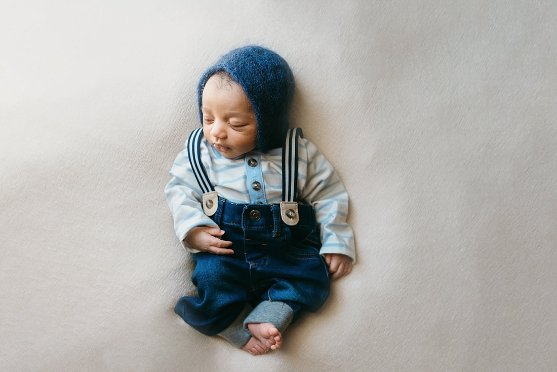 newborn baby boy wearing blue knit bonnet and suspenders for newborn photos in memphis