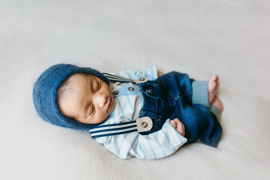 newborn baby boy wearing blue knit bonnet and suspenders for newborn photos in memphis