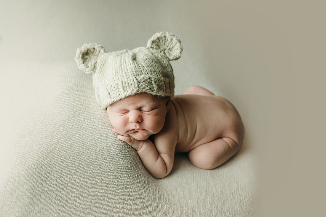 newborn baby boy posed and sleeping on tan blanket, wearing teddy bear hat in Memphis, TN