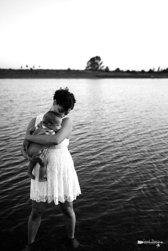 Mother holding baby on the bank of Patriot Lake at sunset at Shelby Farms Park