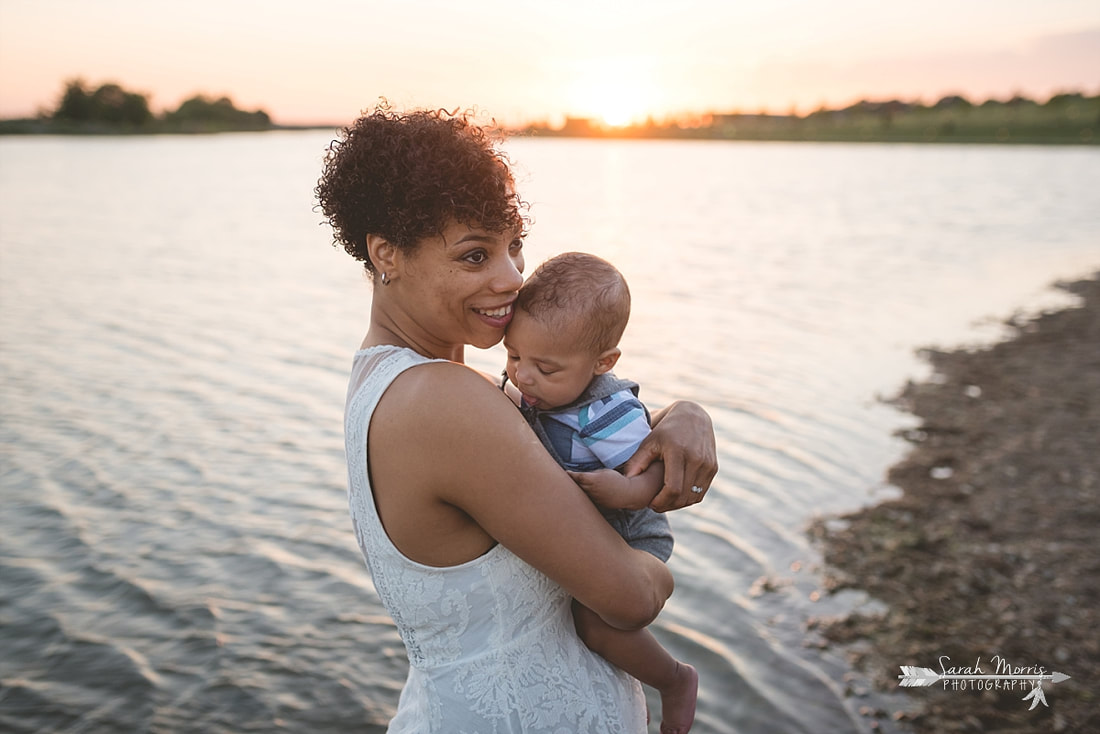Mother holding baby on the bank of Patriot Lake at sunset at Shelby Farms Park