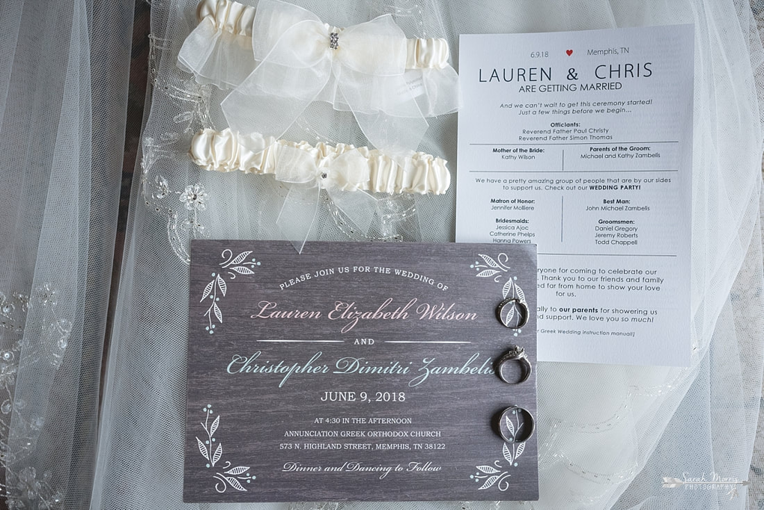 Wedding details: garters, invitation, and wedding rings laying on wedding veil