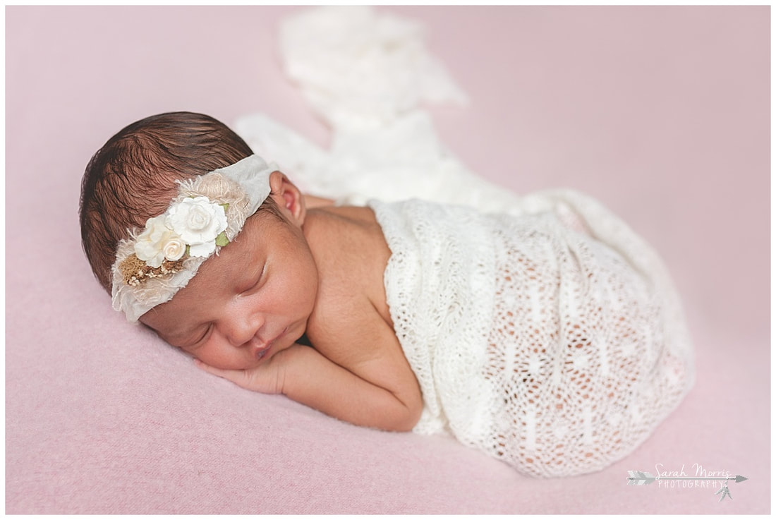 newborn photos of baby girl on pink blanket wearing flower headband