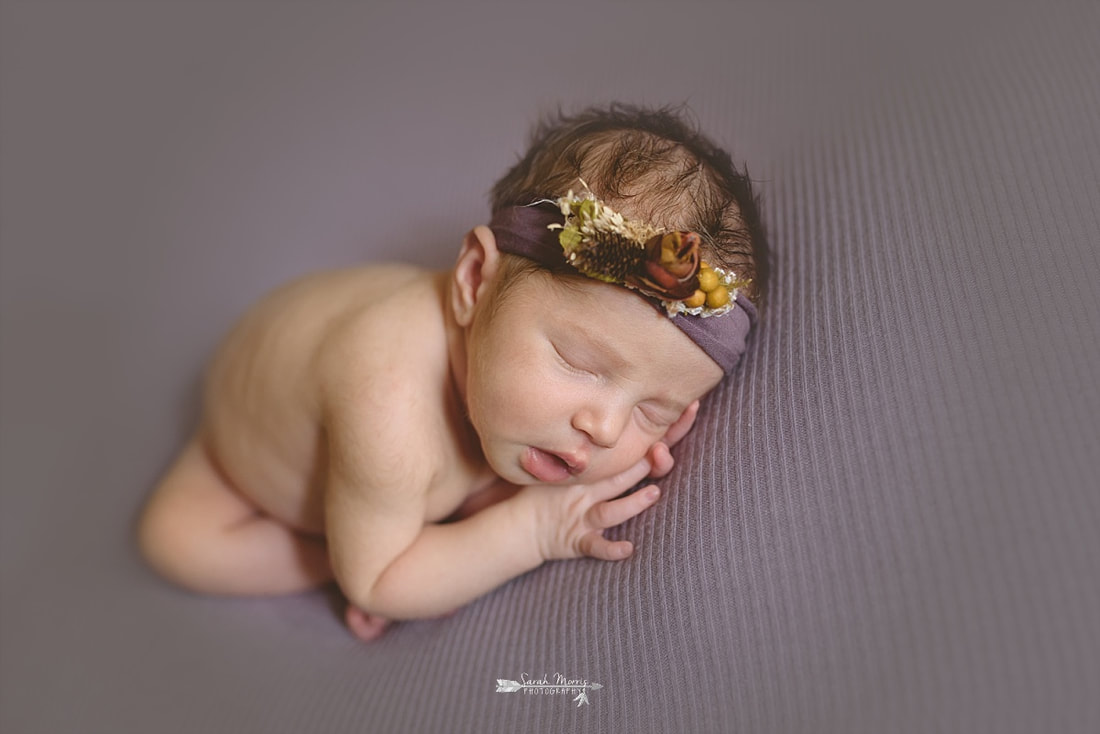 newborn baby girl sleeping on a purple blanket, wearing a purple flower crown