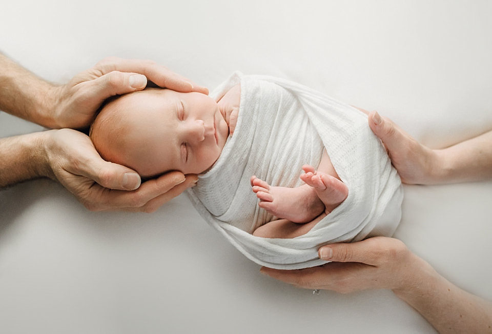 Newborn baby boy sleeping in mother's and father's hands for an infant portrait during newborn photoshoot in Memphis 