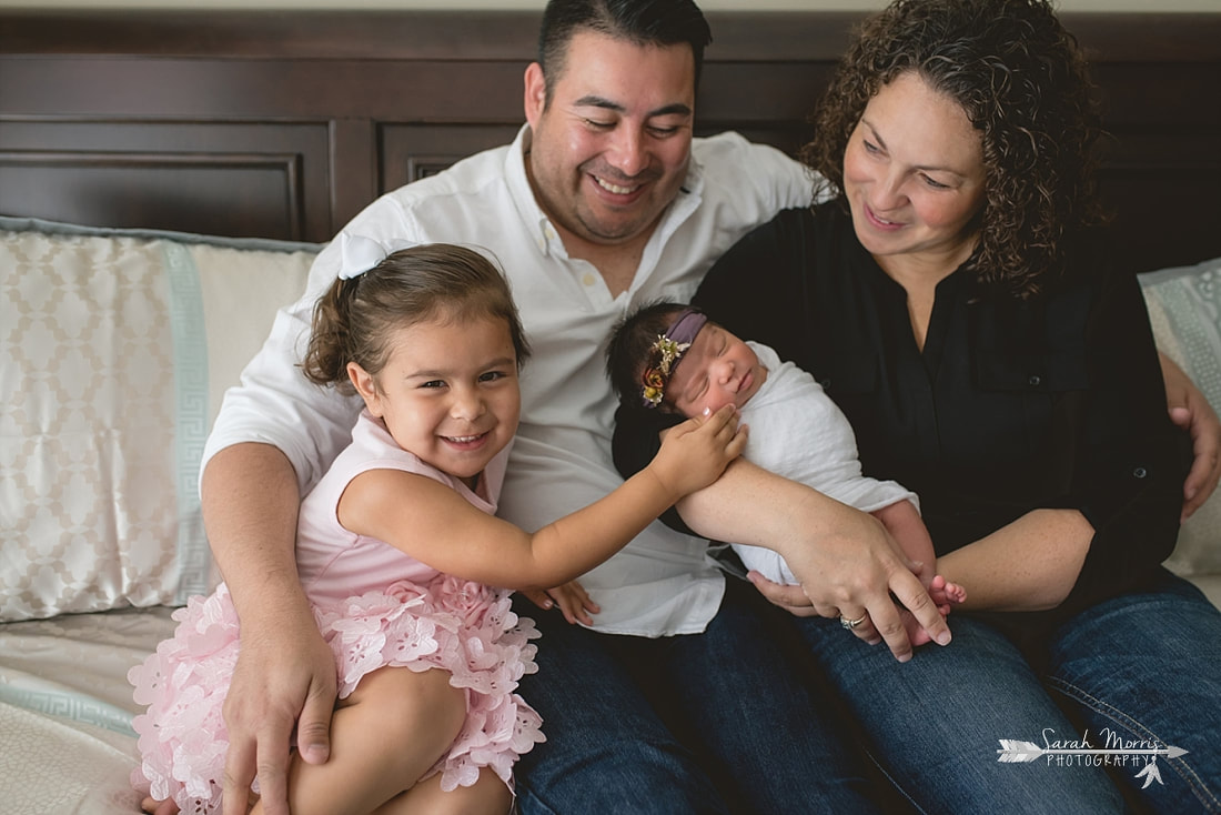 Family cuddled up on bed with newborn baby sister for the lifestyle portion of her newborn photo session