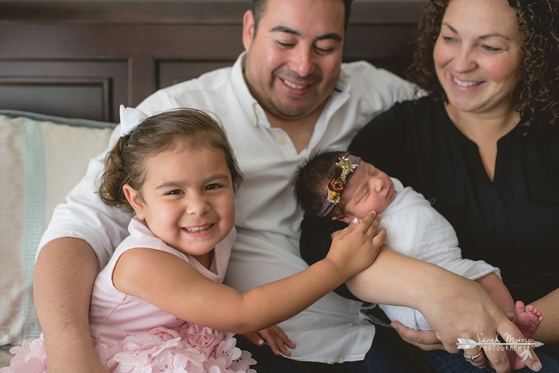 Family cuddled up on bed with newborn baby sister for the lifestyle portion of her newborn photo session