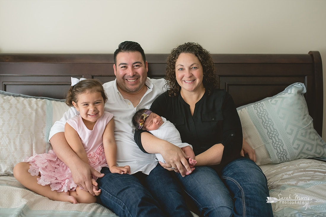 Family cuddled up on bed with newborn baby sister for the lifestyle portion of her newborn photo session