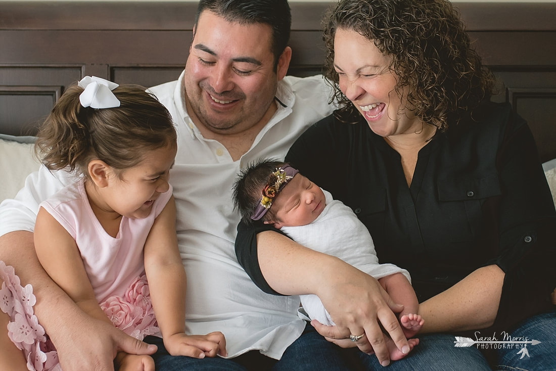 Family cuddled up on bed with newborn baby sister for the lifestyle portion of her newborn photo session