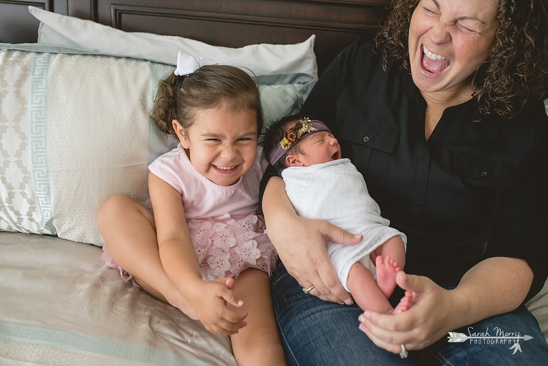 Family cuddled up on bed with newborn baby sister for the lifestyle portion of her newborn photo session