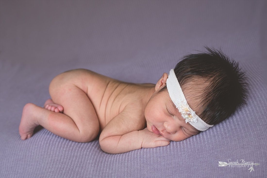 Newborn baby girl wearing a cream headband with pearls sleeping on purple blanket during the posed portion of her newborn session