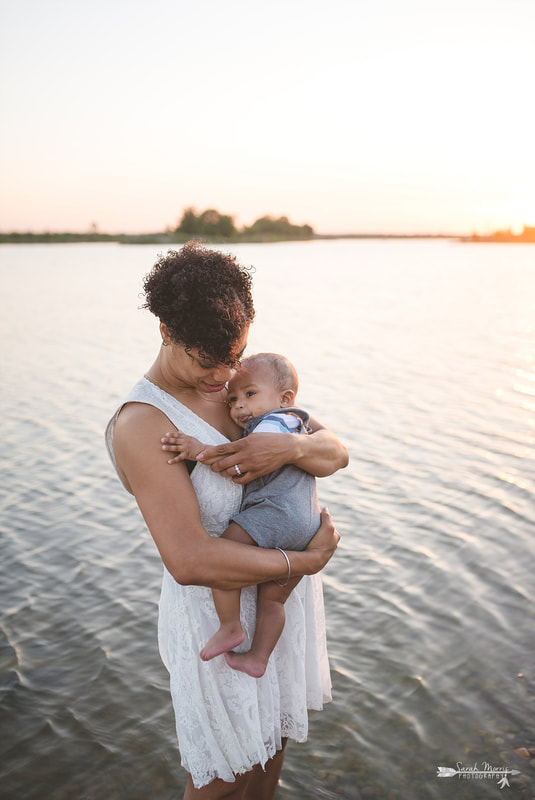 Mother holding baby on the bank of Patriot Lake at sunset at Shelby Farms Park