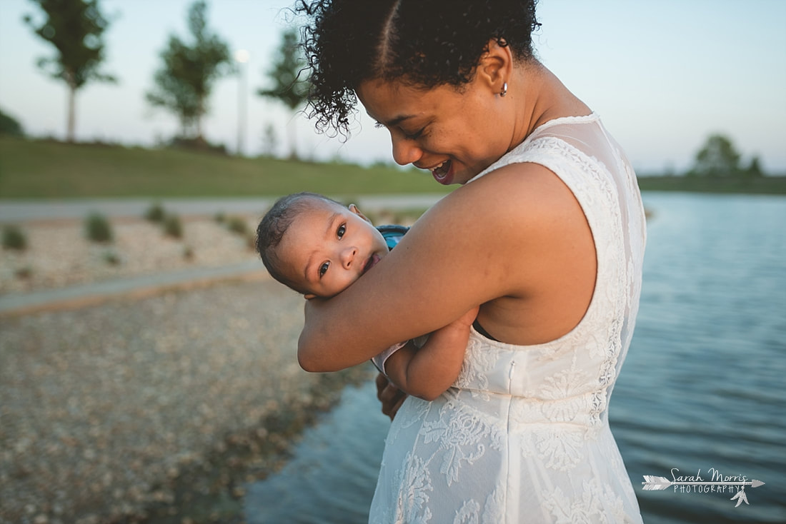 Mother holding baby on the bank of Patriot Lake at sunset at Shelby Farms Park