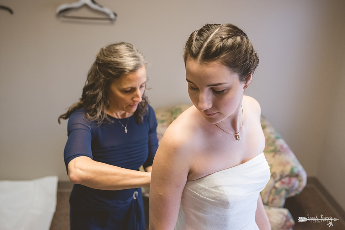 Mother of the bride buttoning bride's wedding dress at St. Francis of Assisi Catholic Church